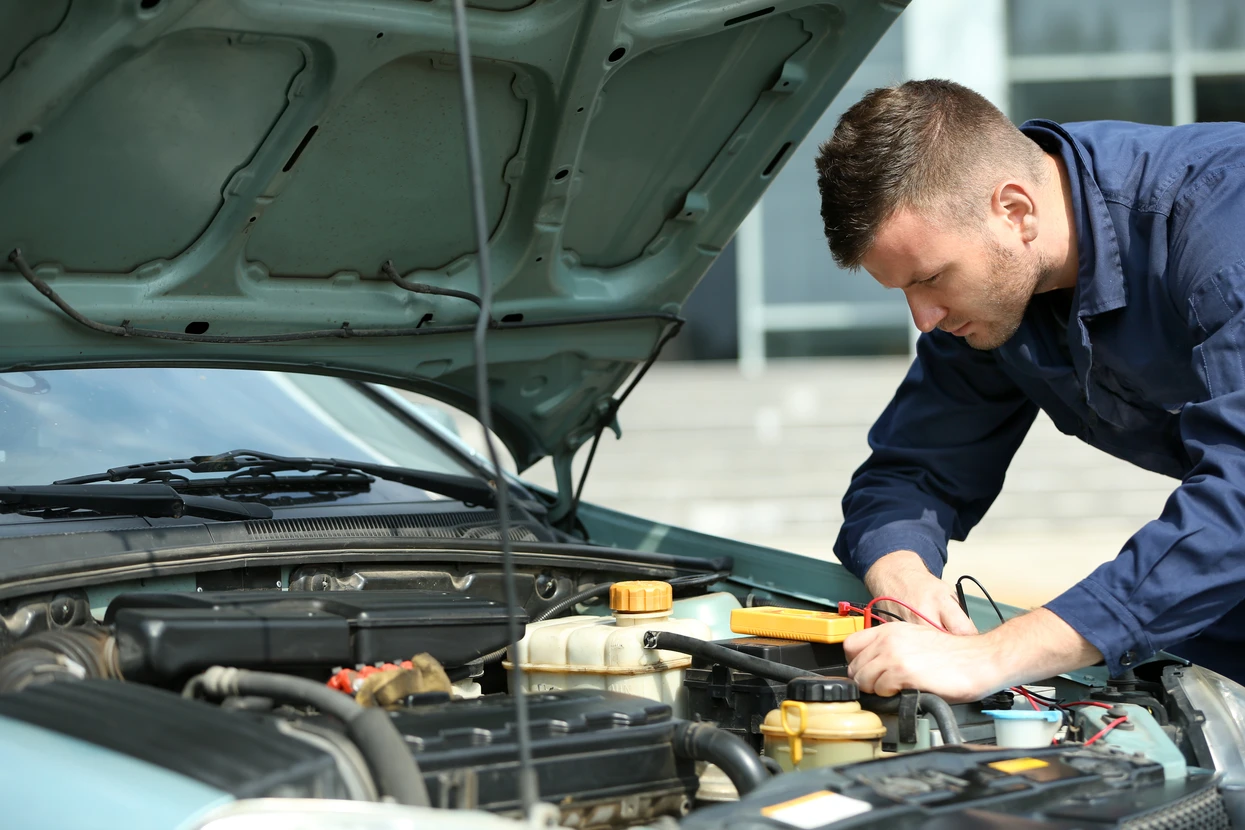 Mécanicien automobile en combinaison bleue travaillant sous le capot ouvert d'un véhicule dans un garage professionnel