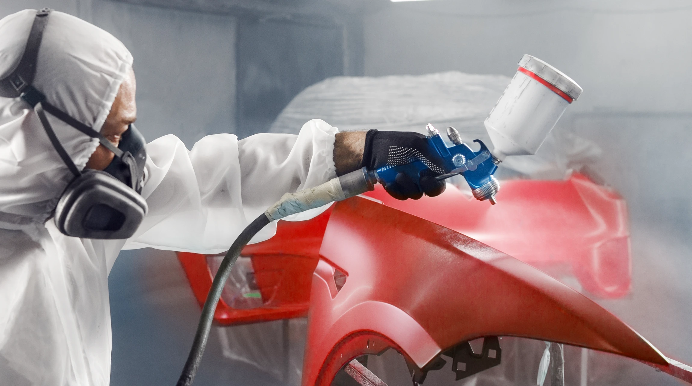 Atelier automobile intérieur, technicien en combinaison grise et rouge utilisant une polisseuse pneumatique sur la carrosserie d'un SUV bleu foncé