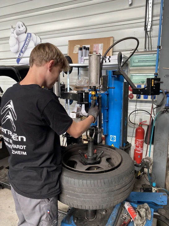 Mécanicien automobile en combinaison bleue gonflant un pneu dans un garage professionnel